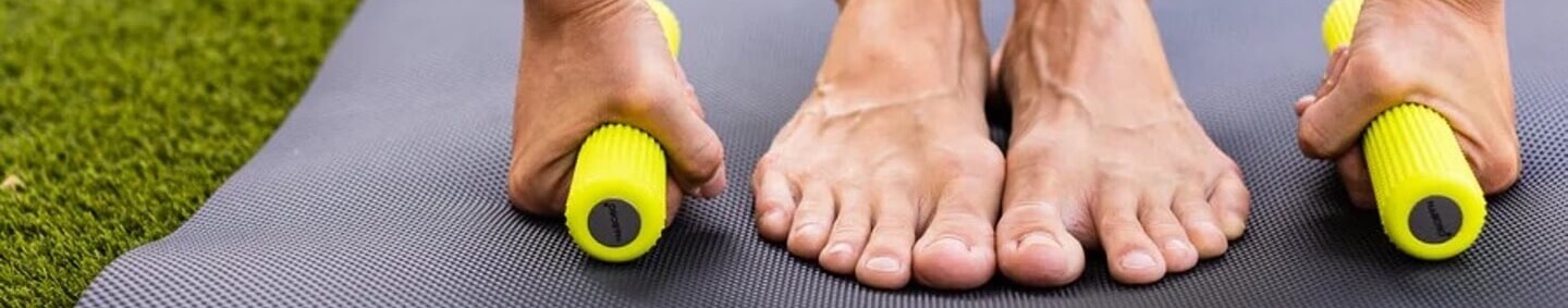 Person uses a bright yellow massage roller on a black exercise mat, feet flat on the mat in a stretch setup